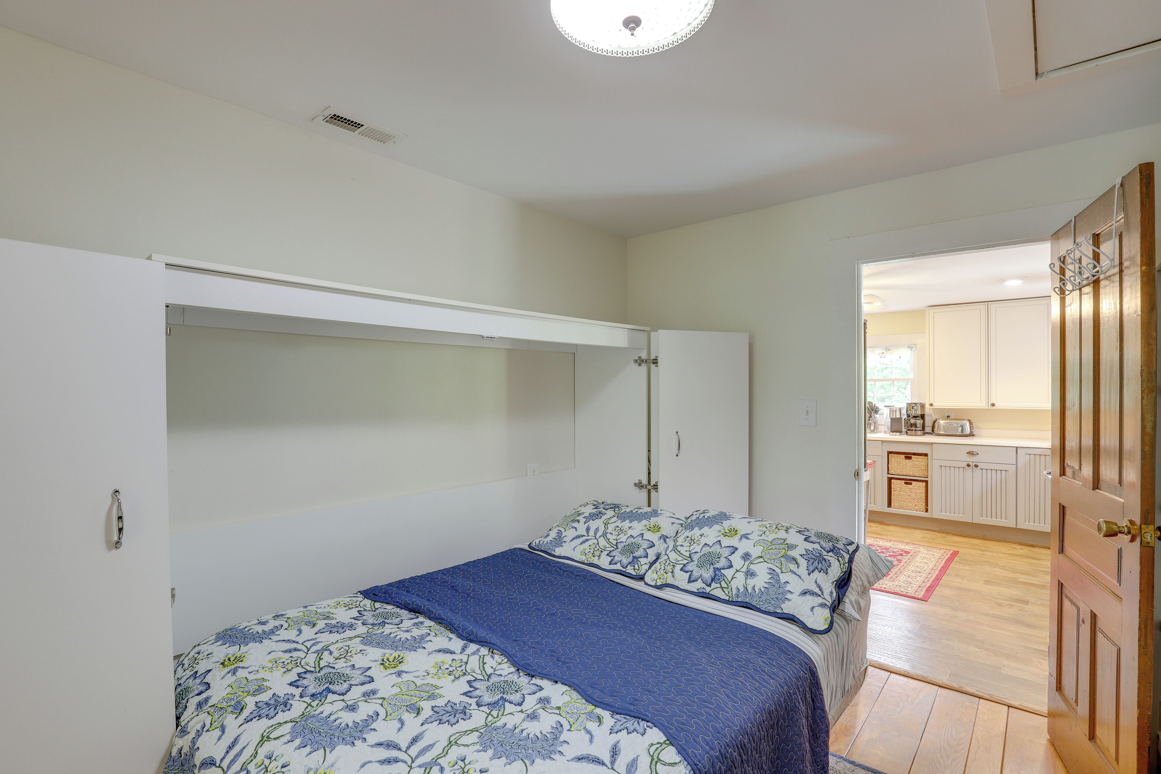 A bedroom with a bed, a wardrobe, and a view into the kitchen.