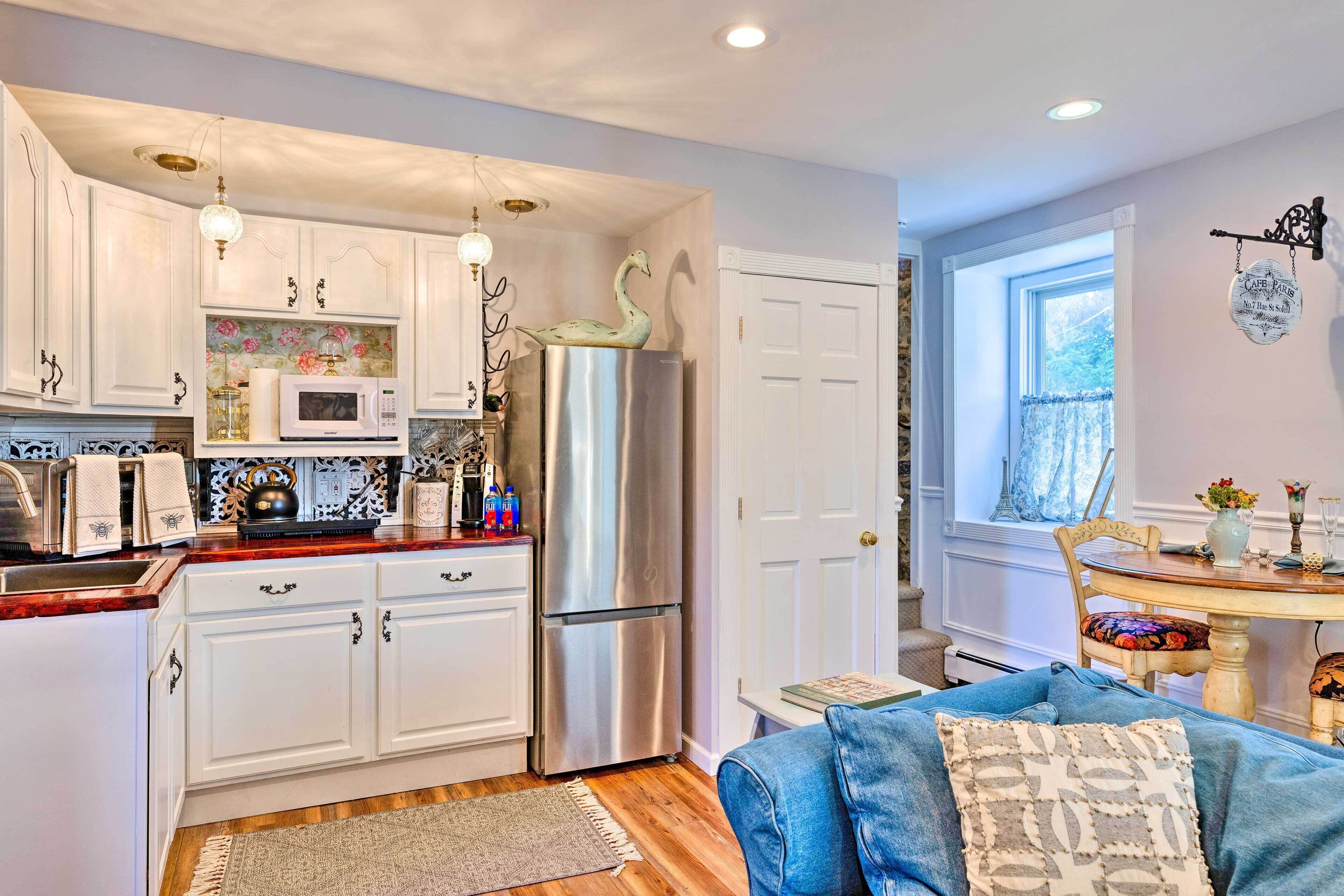 A kitchen with white cabinets, a stainless steel refrigerator, a microwave, and a decorative swan. There is a dining area with a table and chairs, and a window with a view of trees.