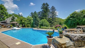A swimming pool with a stone deck, surrounded by lush greenery and a stone wall.