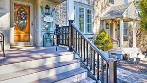 A stone house with a wooden front door, a porch with a railing, and a small gazebo.