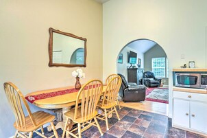 Un comedor con mesa y sillas de madera, un espejo en la pared y una zona de cocina con microondas.