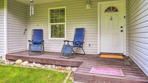 Une véranda avec deux chaises de jardin bleues, une porte blanche et une petite marche menant à l’entrée.