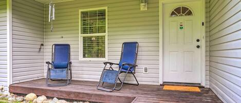 A porch with two blue lawn chairs, a white door, and a small step leading to the entrance.