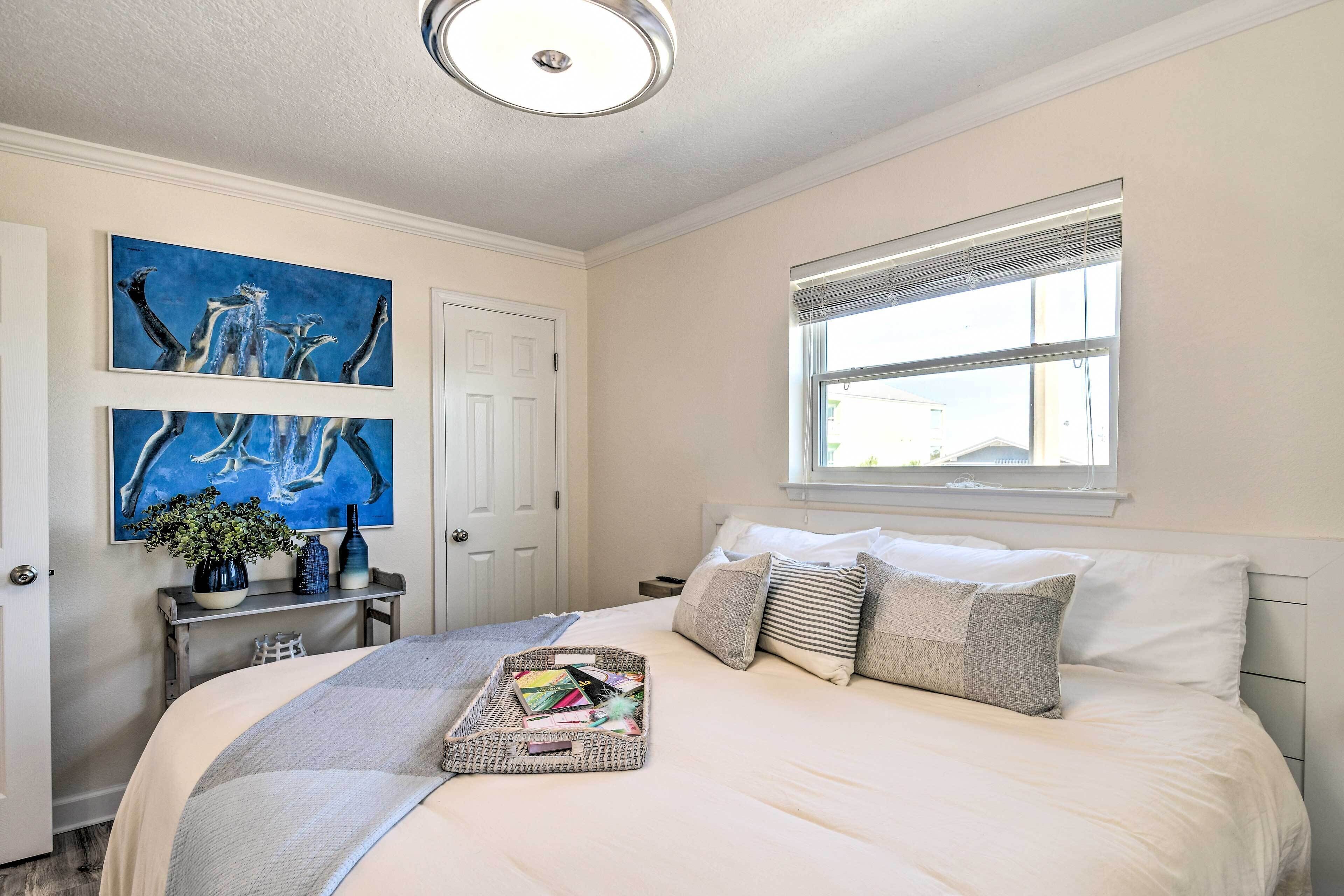 A bedroom with a bed, a window, and artwork on the wall.