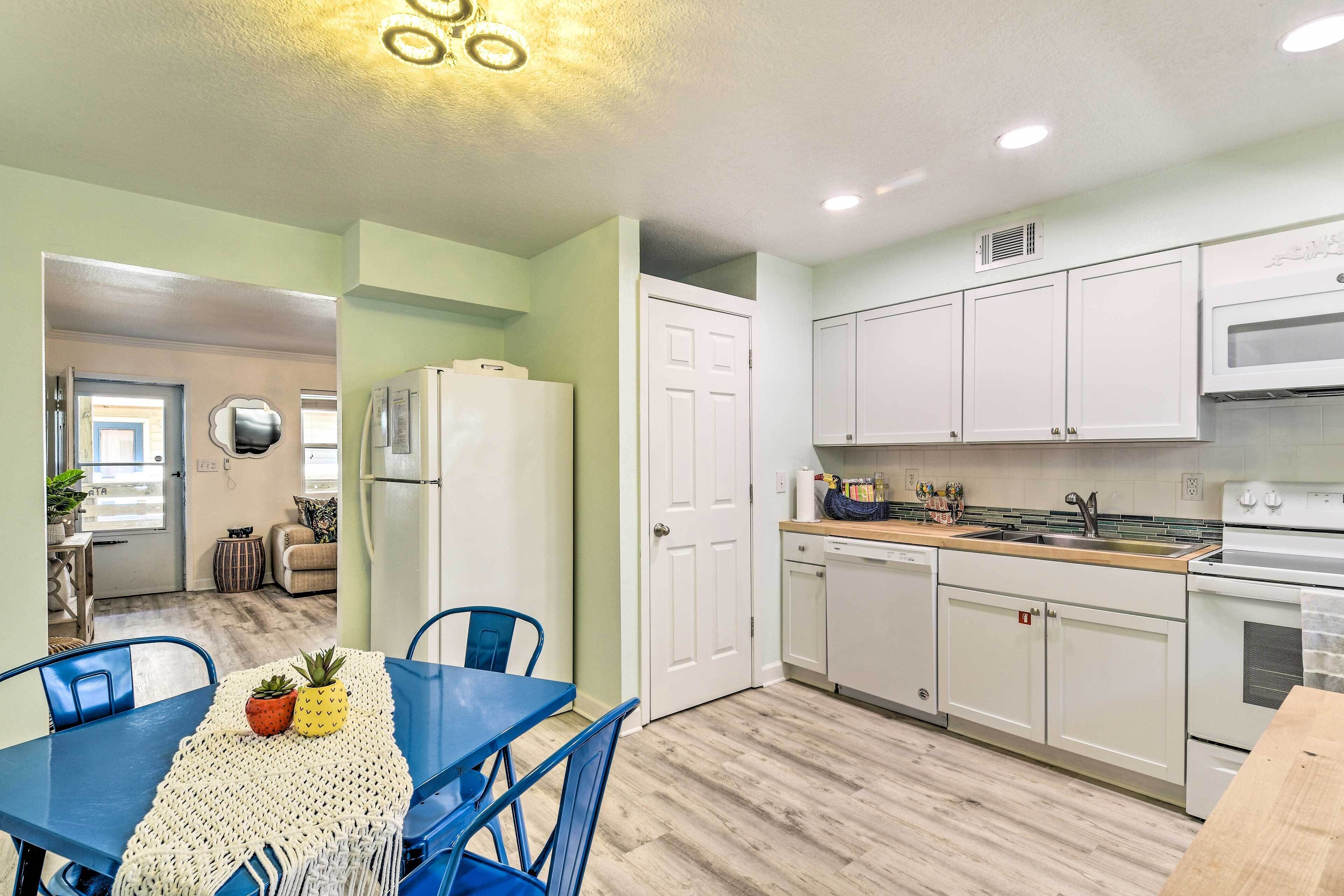 A modern kitchen with white cabinets, a wooden countertop, and a dining area with blue chairs and a table.