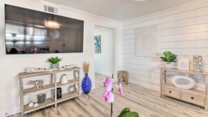 Una sala de estar moderna con un televisor de pantalla plana grande, un mueble bajo de madera, plantas decorativas y una araña.