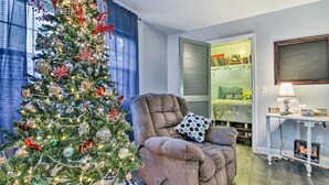 A cozy living room with a large Christmas tree, a comfortable armchair, and a small table with a lamp. - 14 Mi to Frankenmuth: Apt on 3 Acres in Clio! (Clio)