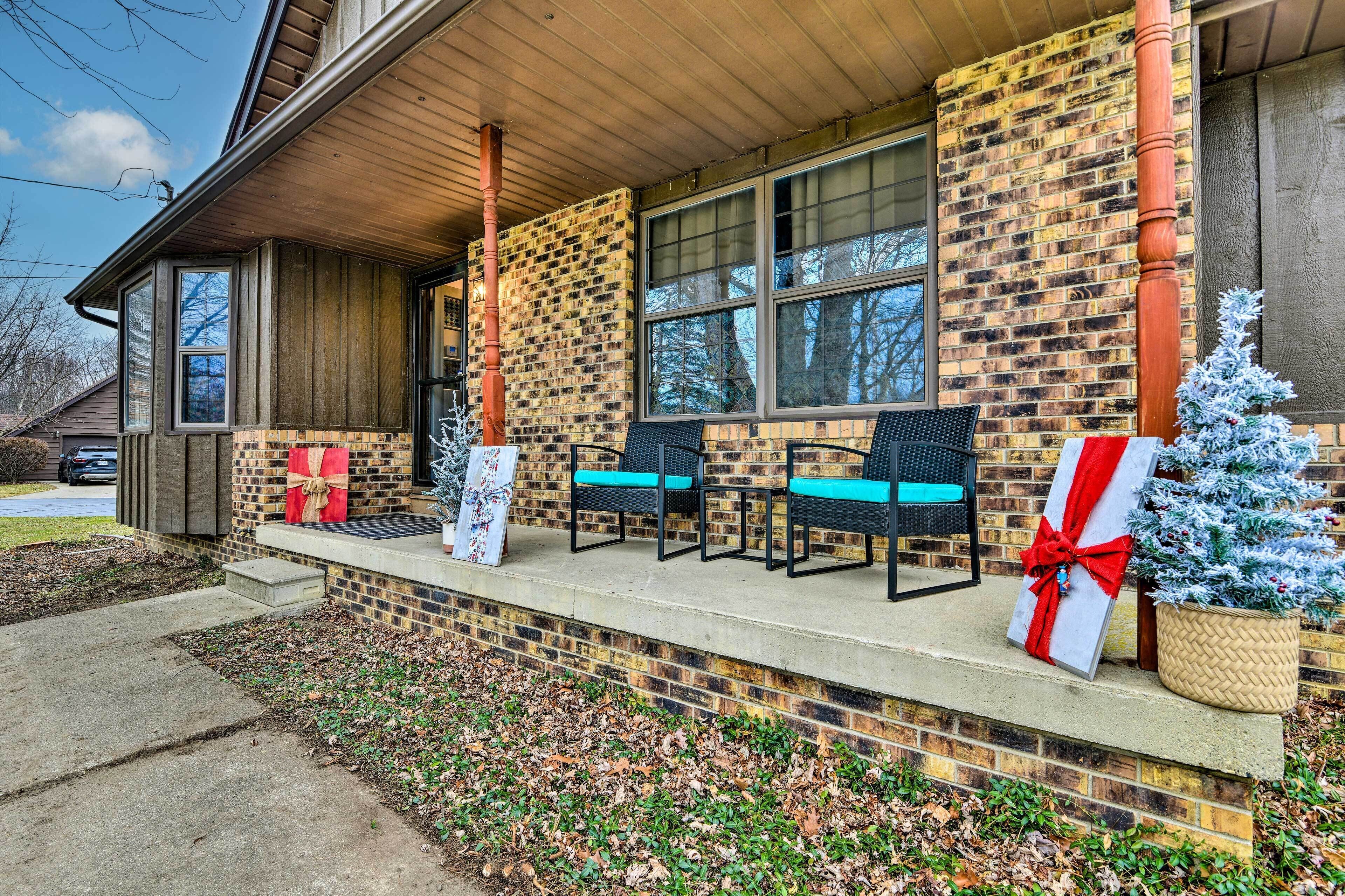 A brick building with a porch, two chairs, a small Christmas tree, and a gift box.