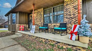 A brick building with a porch, two chairs, a small Christmas tree, and a gift box.