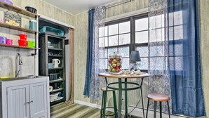 A kitchen with wooden cabinets, a sink, a window with patterned curtains, and a table with stools. - 14 Mi to Frankenmuth: Apt on 3 Acres in Clio! (Clio)