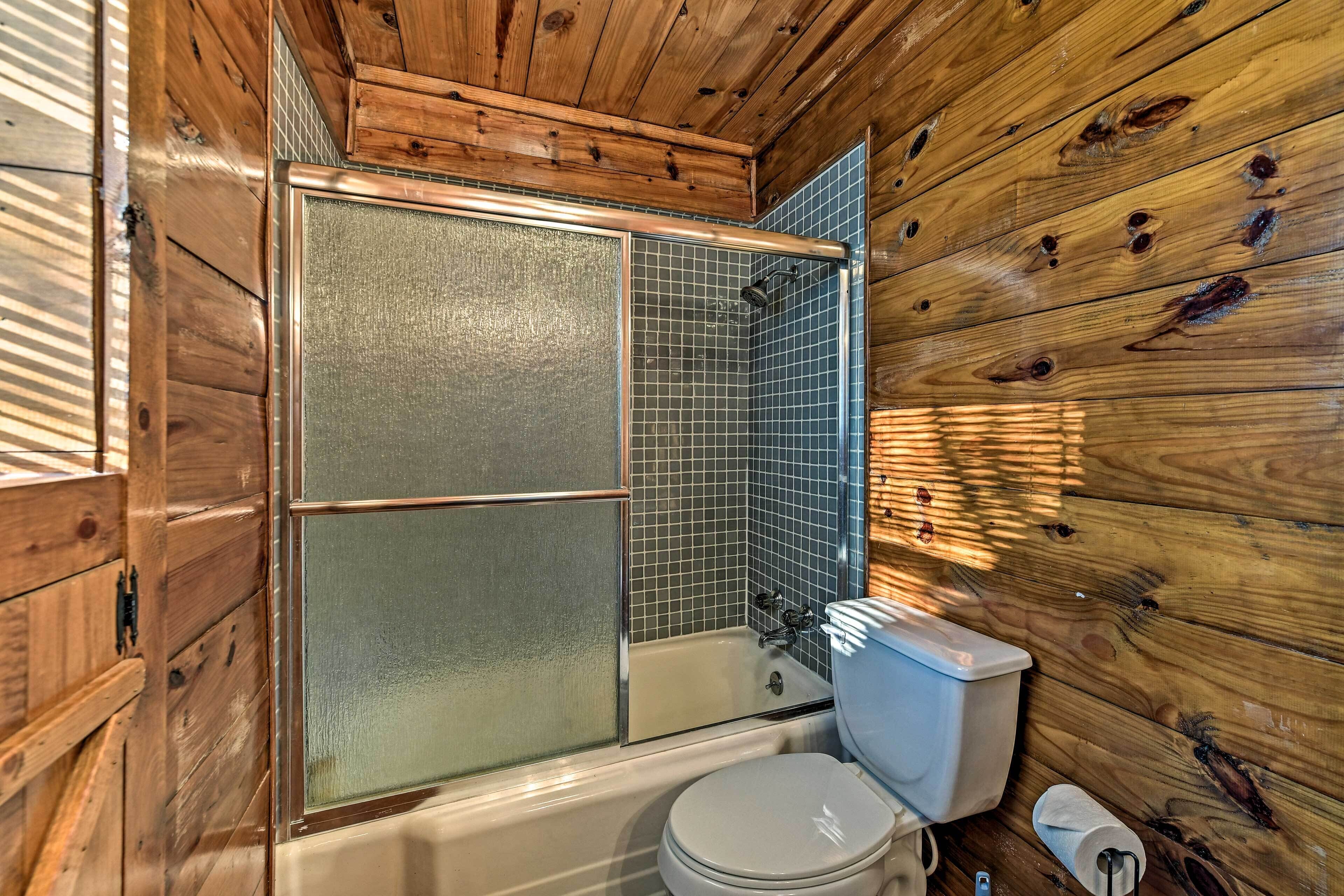 Un baño de cabaña de madera con bañera, inodoro y zona de ducha.