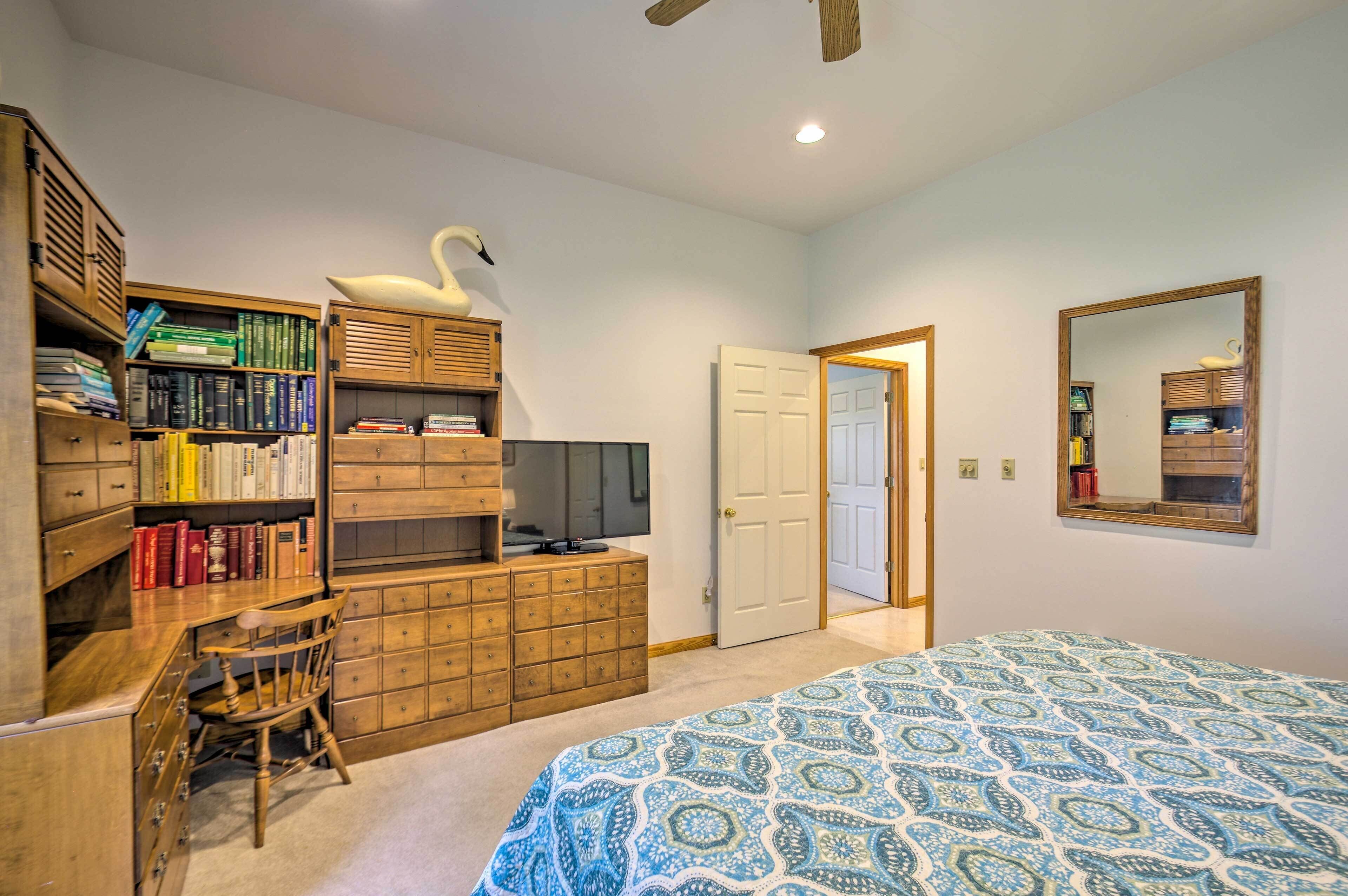 A bedroom with a bed, a wooden dresser, a television, and a bookshelf.
