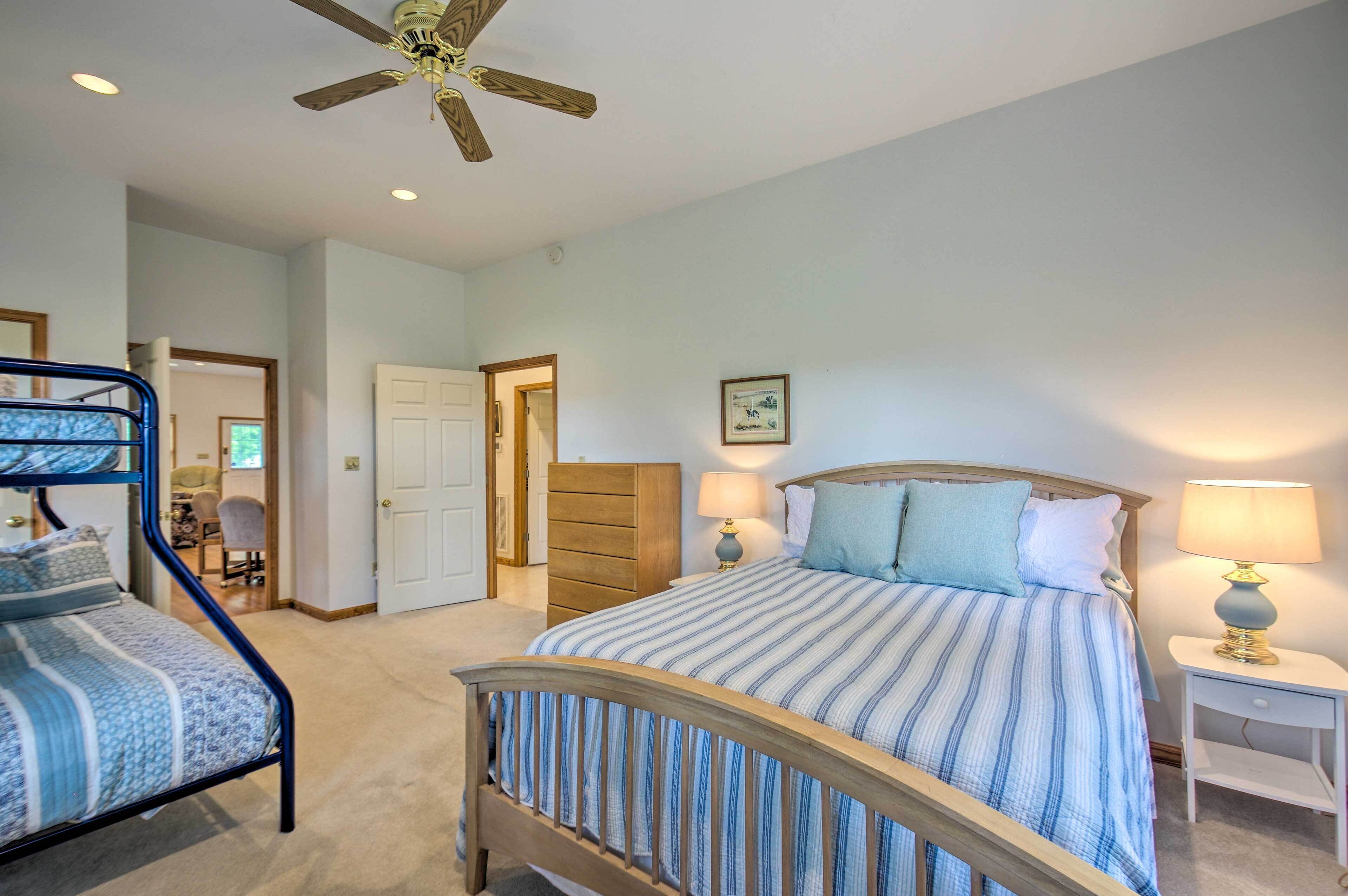 A bedroom with a bed, two bedside tables, a ceiling fan, and a door leading to another room.