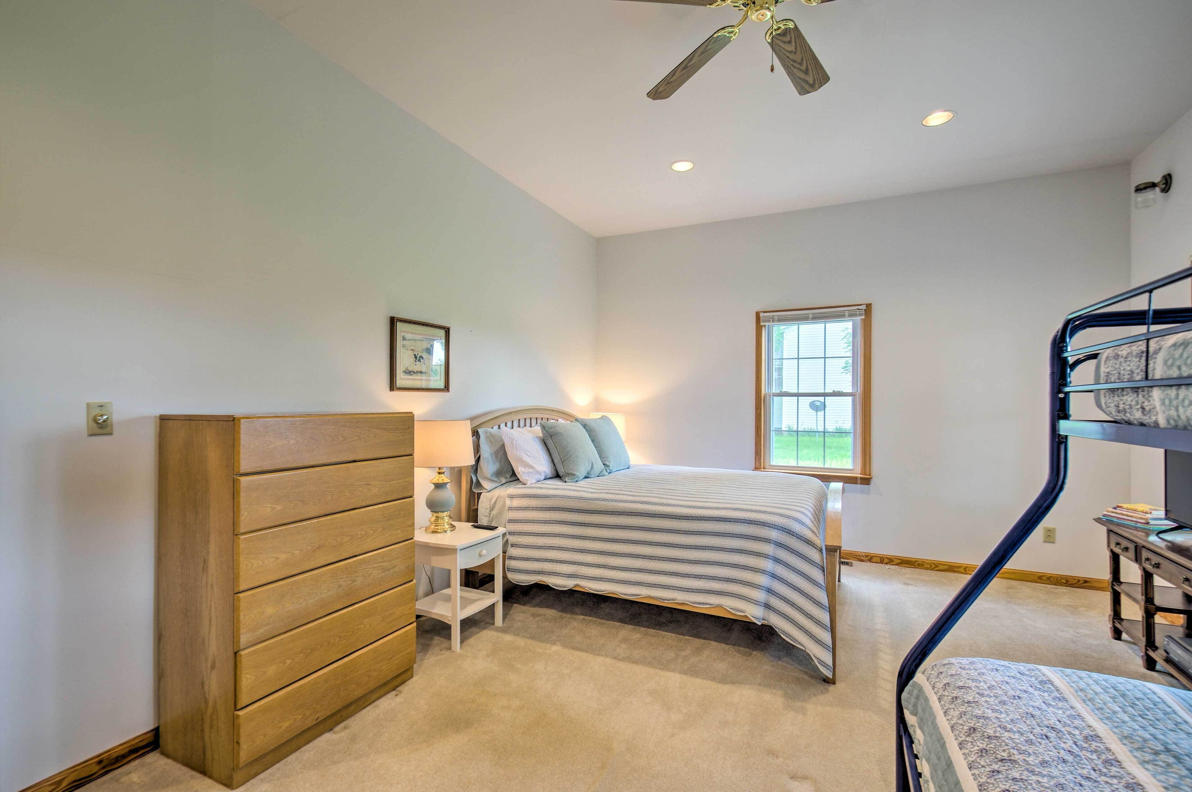 A bedroom with a bunk bed, a bedside table with a lamp, a window with a view, and a ceiling fan.