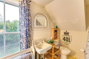 A bathroom with a window, a sink, a mirror, a toilet, and a shelf with toiletries.