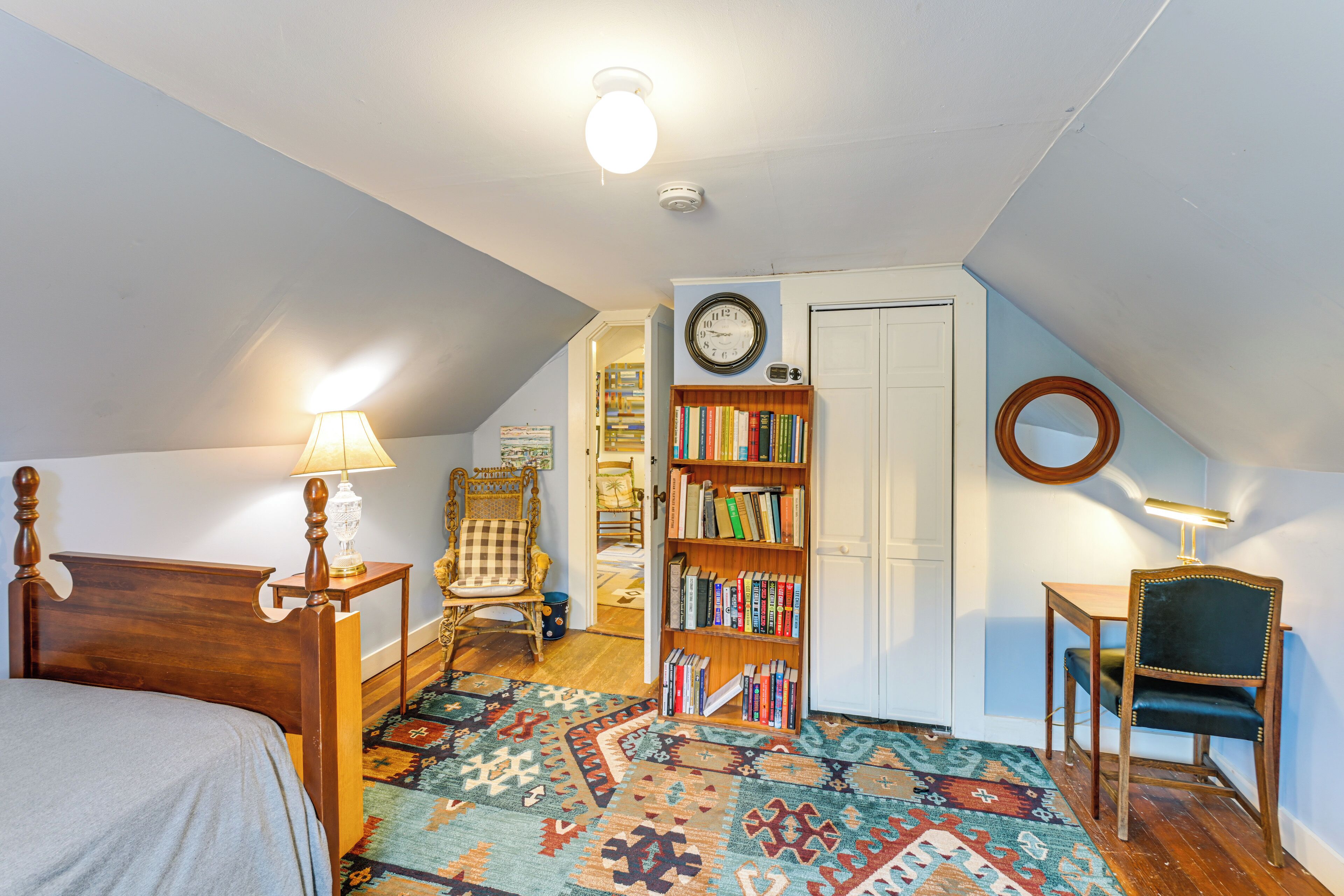 A bedroom with a bed, a bookshelf, a chair, a desk, and a patterned rug.