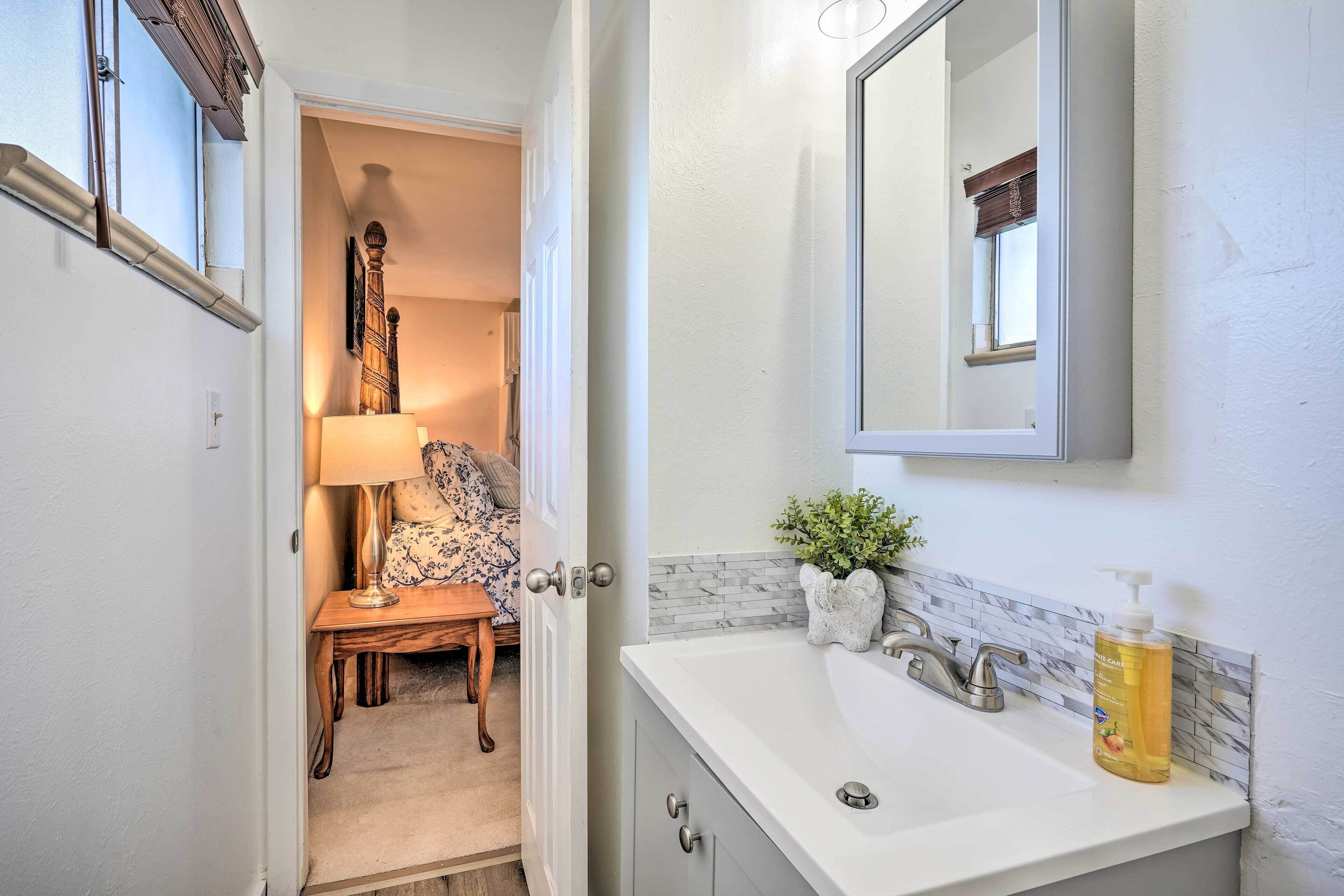 A bathroom with a white sink, a mirror above it, and a bottle of shampoo on the counter.