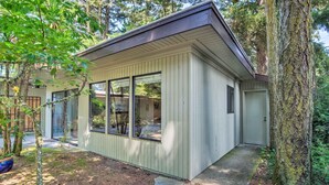 A small, single-story building with large windows and a sloped roof, surrounded by trees and a stone pathway. - Coos Bay Cottage w/ Fireplace & BBQ Patio! (Coos Bay)