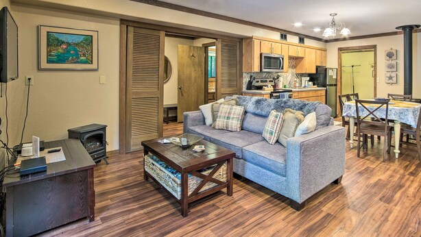 A living room with a sofa, coffee table, and a fireplace. There is a kitchen area with cabinets and appliances. - Coos Bay Cottage w/ Fireplace & BBQ Patio! (Coos Bay)