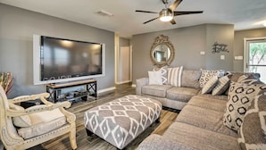 A living room with a flat-screen TV, a ceiling fan, a sofa, an ottoman, and a decorative mirror. - Dog-friendly Texas Retreat w/ Hot Tub, Patio & Bar (Converse)
