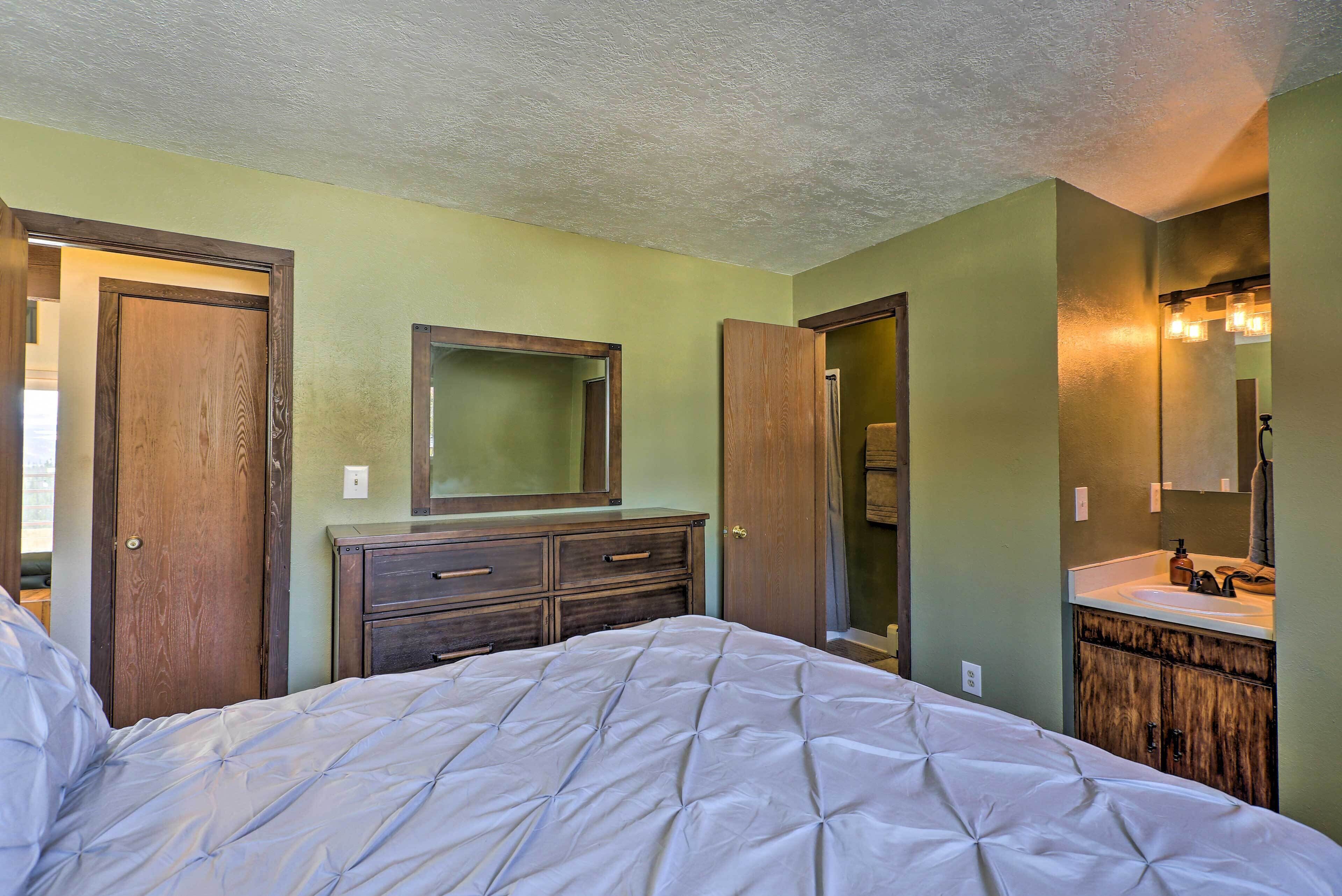A bedroom with a bed, wooden dresser, and a bathroom with a sink and mirror.