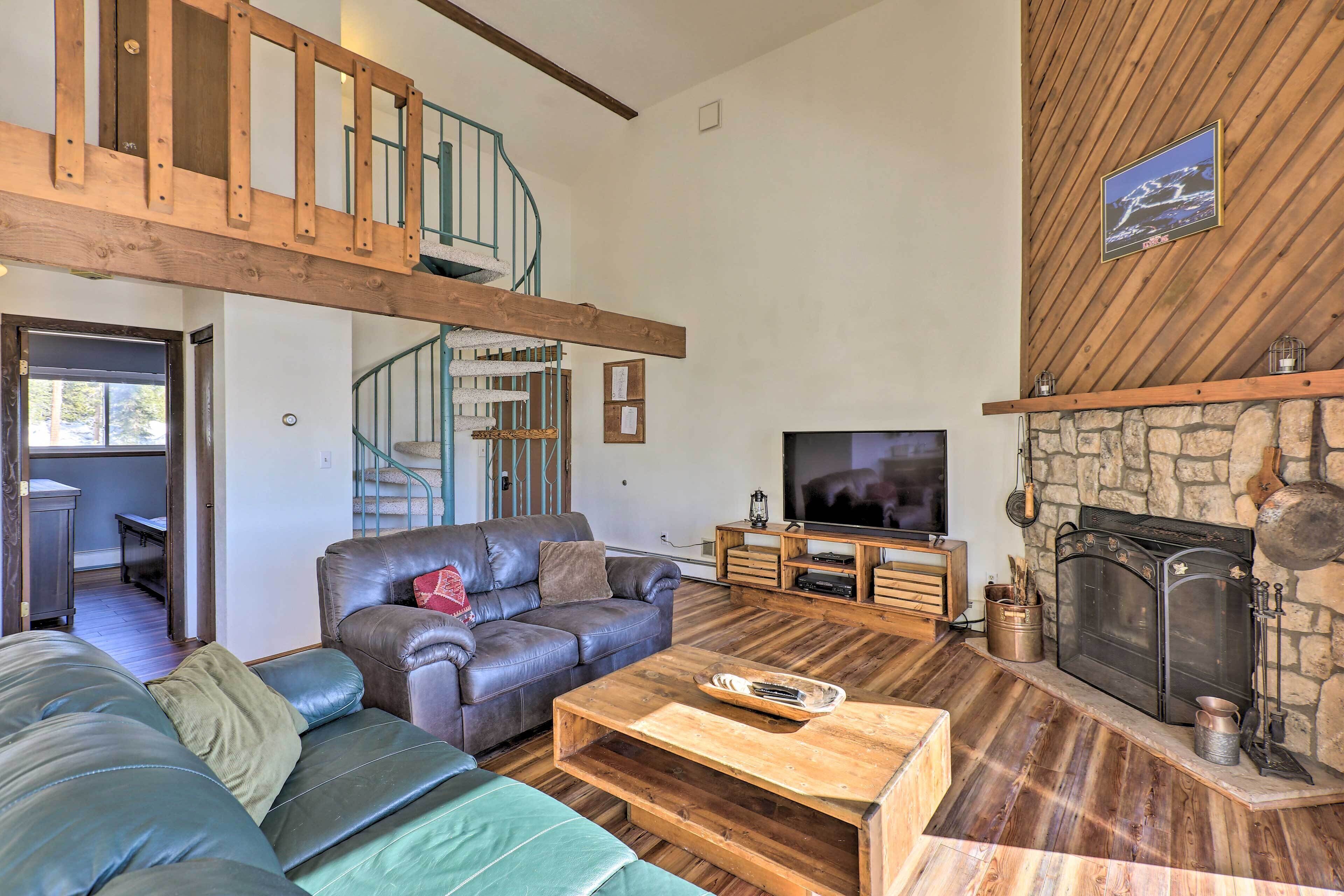 Amplia sala de estar con techo de madera alta, chimenea de piedra, televisor y sofás de cuero.