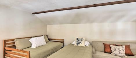 A room with two beds, one wooden and one with a headboard, and a sofa with patterned cushions.