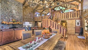 A spacious interior with a wooden dining table, a stone wall, a fireplace, and a wooden staircase. - Countryside Cabin Retreat w/ Outdoor Kitchen! (Rienzi)
