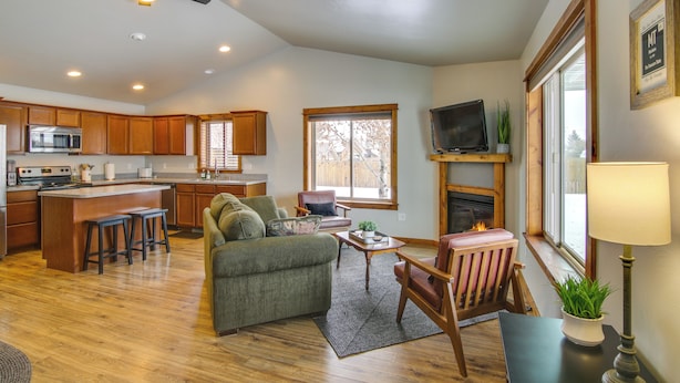 A spacious living room with a green sofa, wooden coffee table, and a fireplace. A kitchen with wooden cabinets and a microwave is visible in the background. - Cozy Belgrade Home Near Skiing, Hiking & Airport! (Belgrade)