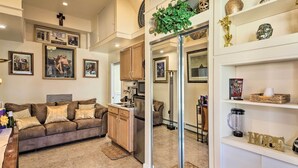 A modern living room with a sofa, kitchen area, and a glass door leading to another room.