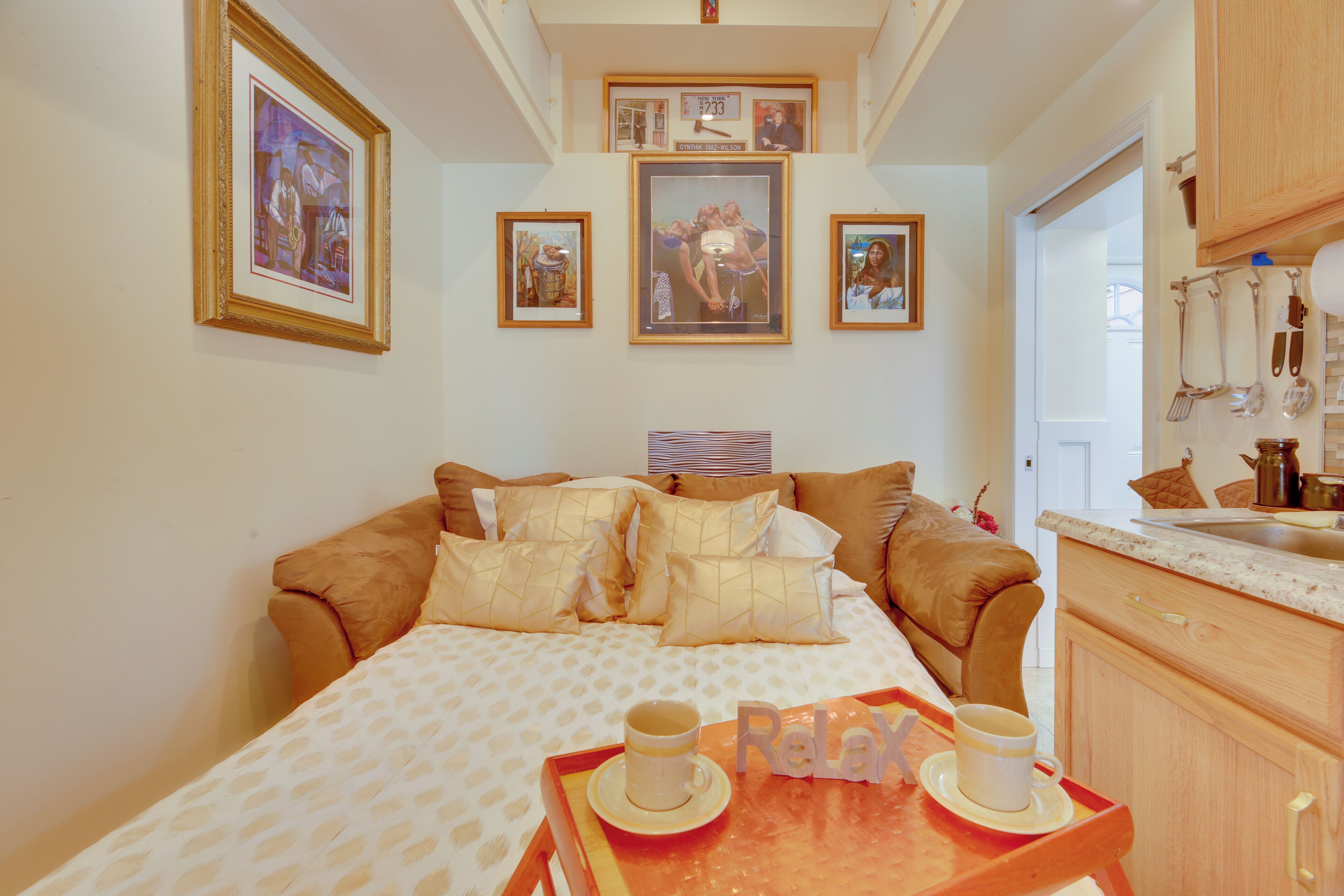 Un dormitorio con cama, una mesita de noche con dos tazas y una bandeja. Hay cuadros en la pared.