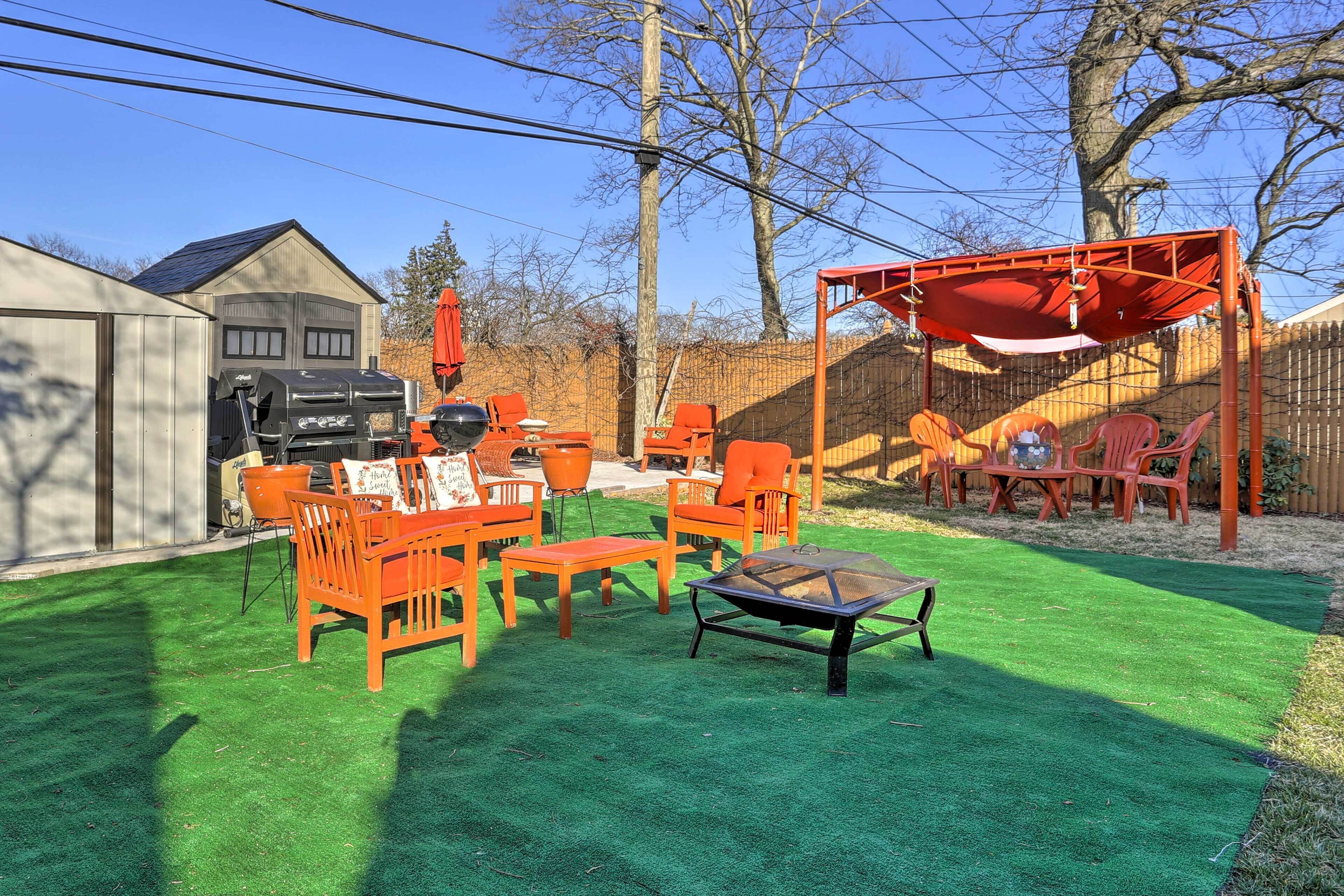 Un jardin avec une pelouse artificielle verte, des meubles de patio orange, un barbecue et une structure en forme de tonnelle rouge.