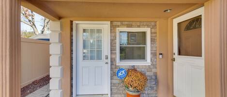 A house entrance with a white door, a welcome mat, a potted plant, and a blue sign.