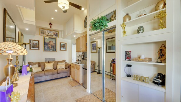 A spacious living room with a sofa, coffee table, and decorative items. There is a kitchen area with cabinets and a refrigerator.