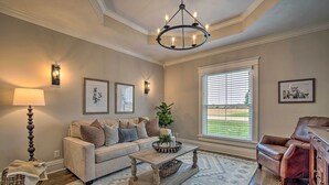 A living room with a sofa, a coffee table, a leather chair, a chandelier, and framed artwork on the walls. - Countryside Cottage w/ Large Yard Near Topeka (Silver Lake)