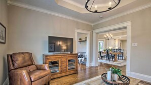 A living room with a leather armchair, wooden entertainment center, and a dining area with a chandelier. - Countryside Cottage w/ Large Yard Near Topeka (Silver Lake)