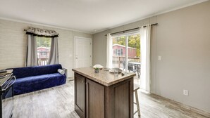Eine moderne Küche mit einer zentralen Kochinsel, einem blauen Sofa und Blick auf ein rotes Haus durch das Fenster.
