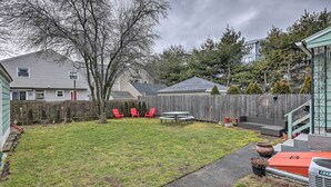 A backyard with a wooden fence, a picnic table, and red chairs. - Bridgeport Vacation Rental - Walk to Beach! (Bridgeport)