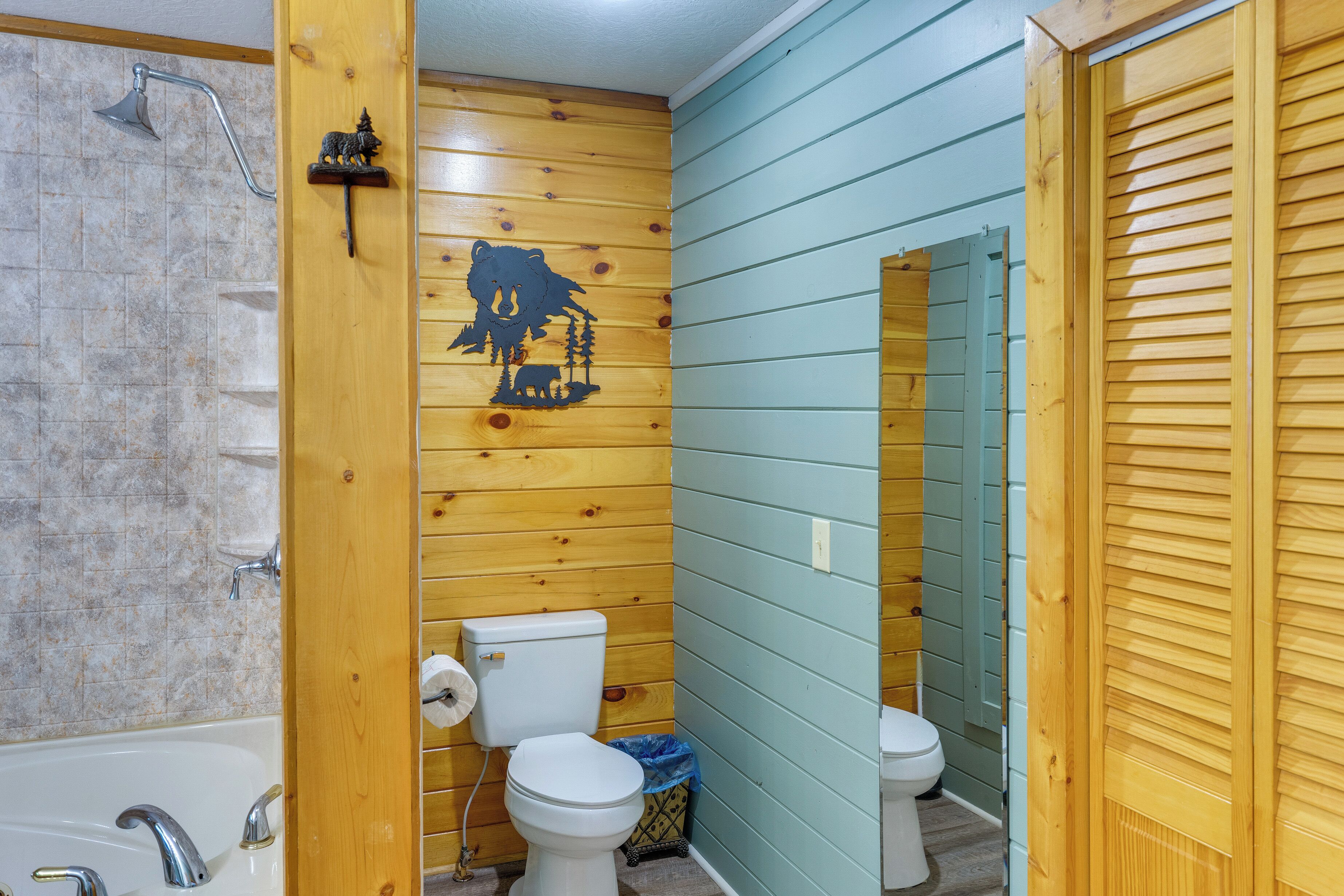 A bathroom with wooden walls, a bathtub, two toilets, and a shower.