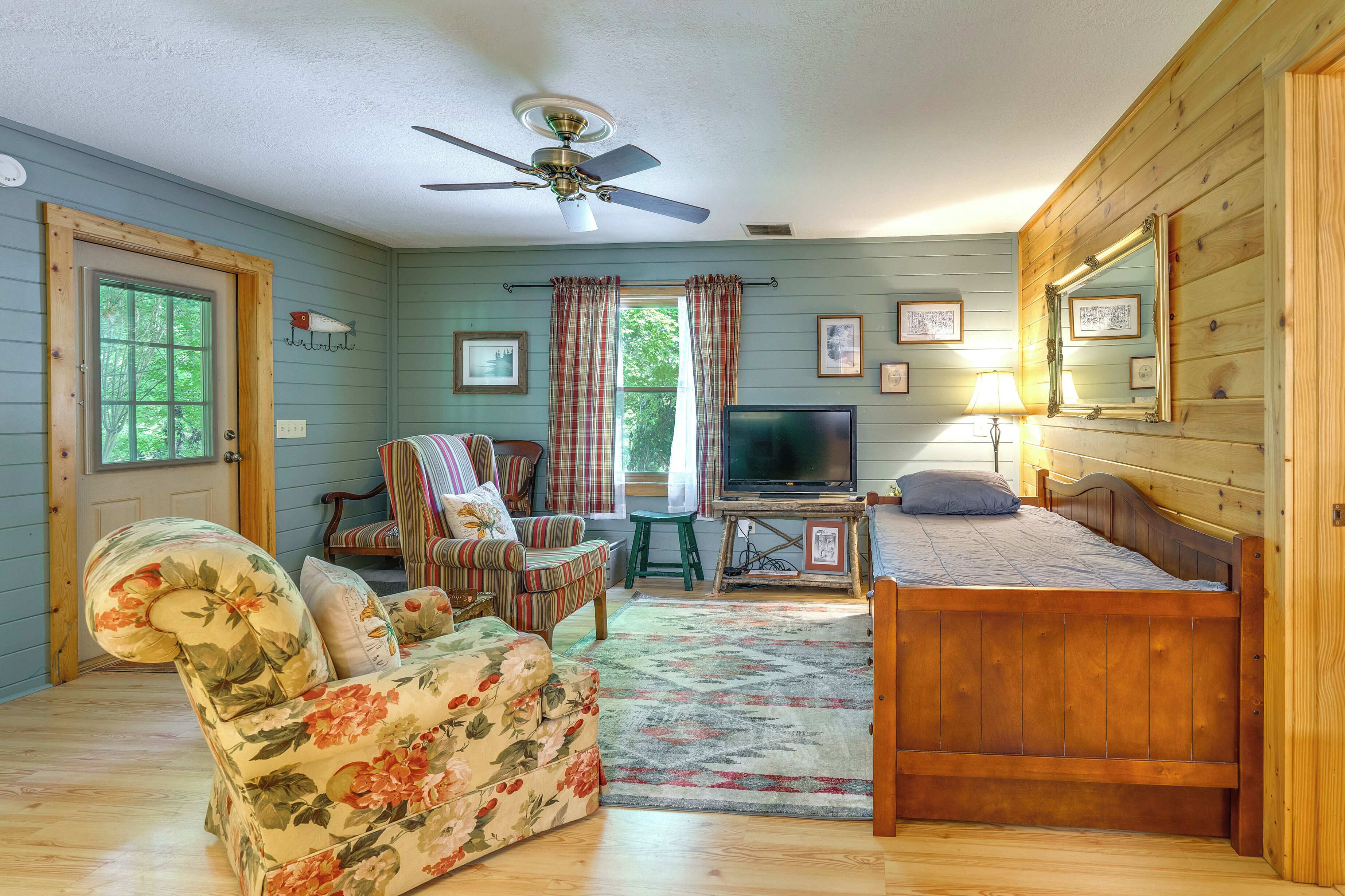 Ein gemütliches Zimmer mit einem hölzernen Bett, einer floralen Couch, einem Fernseher und einem Deckenventilator.