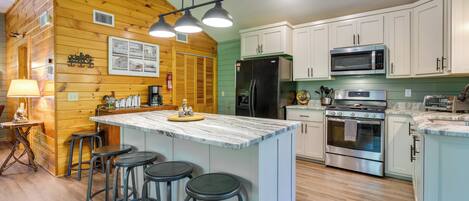 A kitchen with wooden walls, a marble island, bar stools, a refrigerator, a microwave, an oven, and a sink.