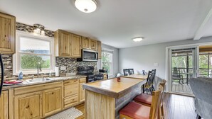 Una cocina con armarios de madera, microondas, lavamanos y una barra con taburetes.