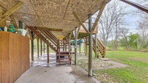 Un espacio al aire libre cubierto, con suelo de concreto, escaleras de madera y una terraza de madera.