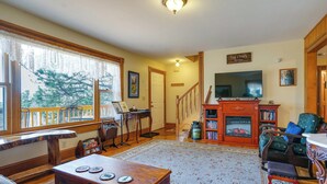 A cozy living room with a fireplace, a television, and a staircase leading to another level. - 'dragons Roost' Cabin w/ Sangre de Cristo Views! (Florissant)