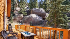 A wooden deck with outdoor furniture, a fire pit, and a view of surrounding rocks and trees. - 'dragons Roost' Cabin w/ Sangre de Cristo Views! (Florissant)