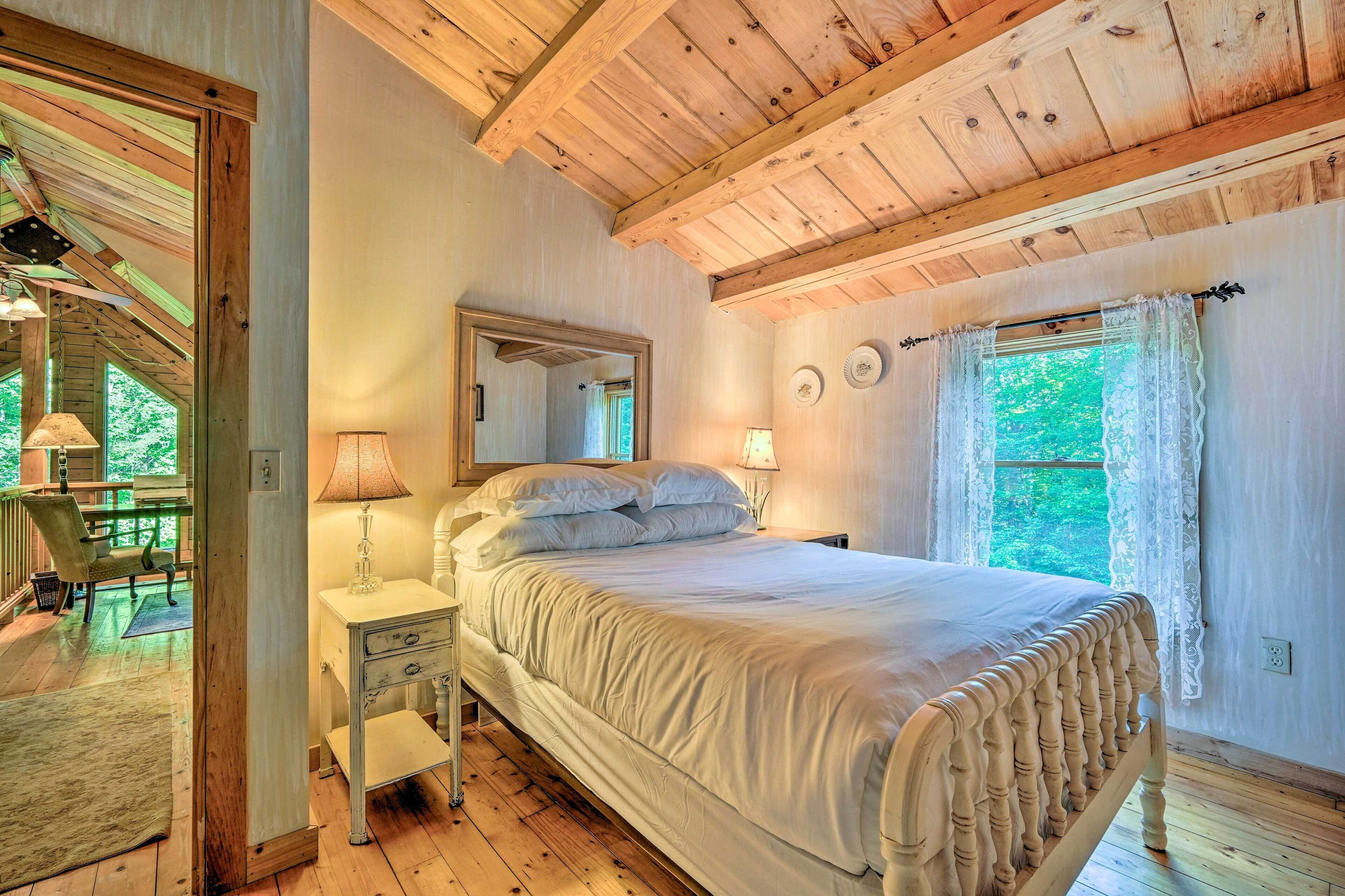 Una camera da letto con un letto di legno, un comodino, una lampada, uno specchio e una finestra con tende di pizzo.