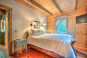 Ein Schlafzimmer mit Holzwänden, einem Bett, Nachttischlampen, einem Fernseher und einem Fenster mit Vorhängen.