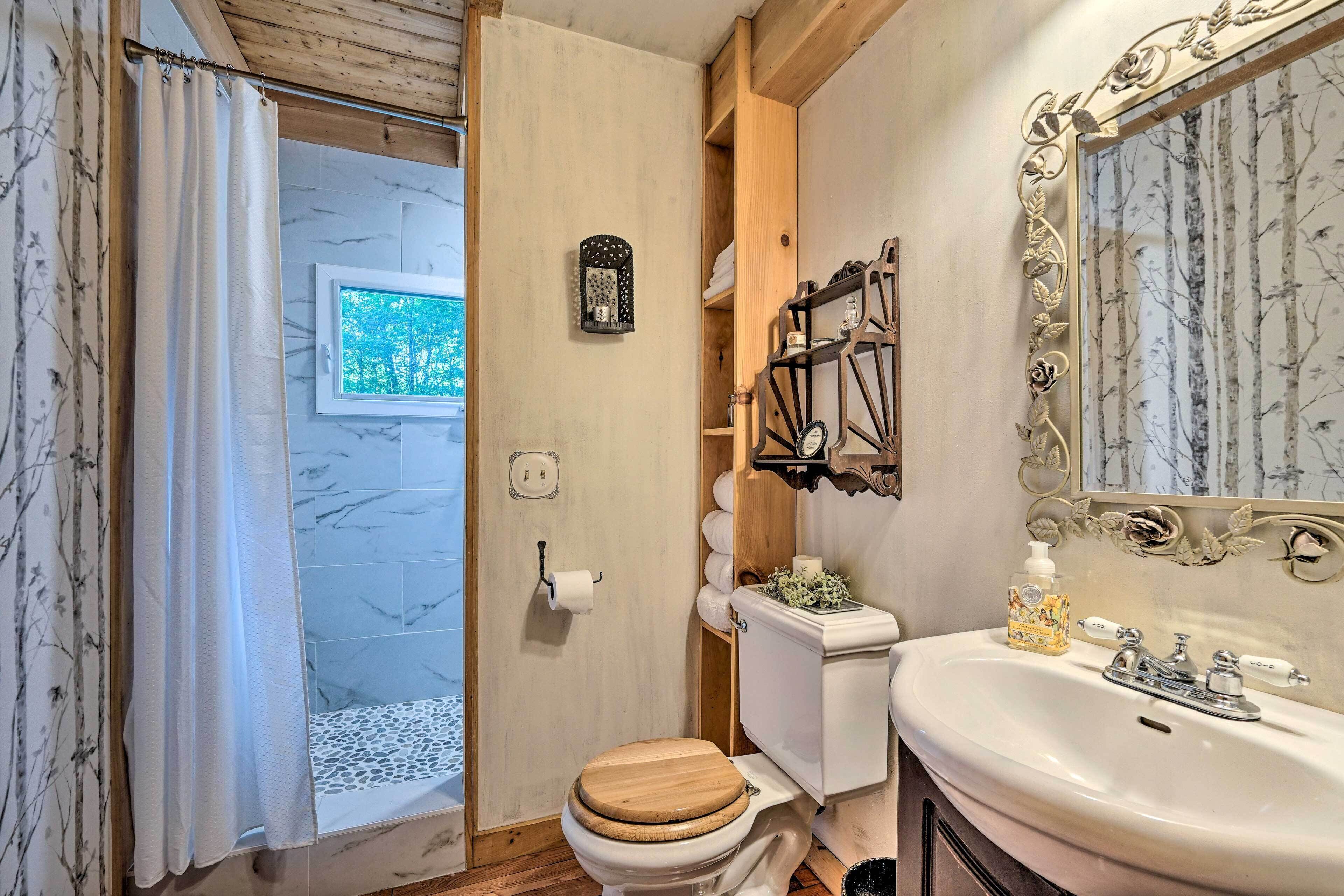Un bany amb vàter de fusta, un lavabo blanc i una zona de dutxa.