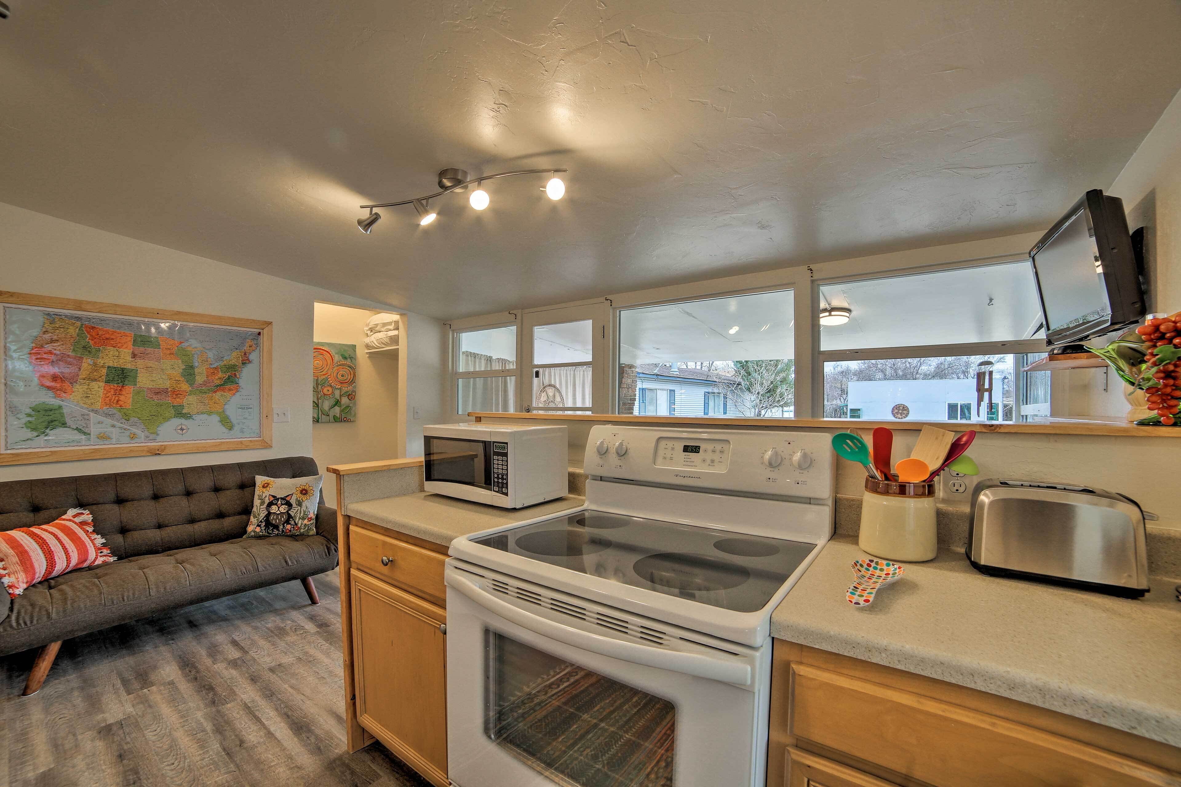 A compact kitchen with a microwave, stove, and toaster. There is a sofa with a map and a painting on the wall.