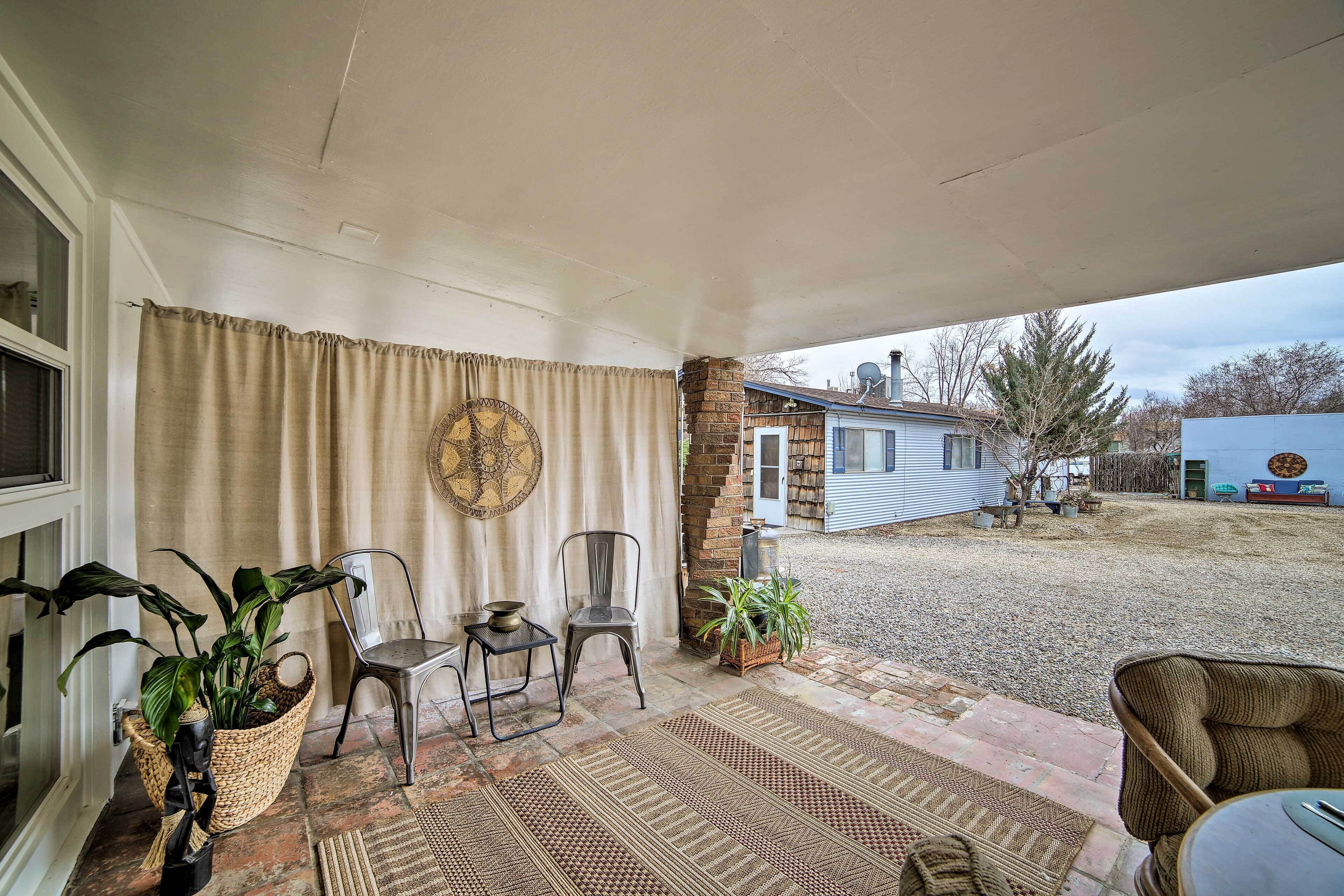 A covered patio area with a view of a house, a brick pillar, and a gravel yard.